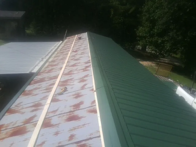Old rusted panels beside newly installed green metal roofing — Wind Damage Roof Repair by Roofing Brothers in Burden