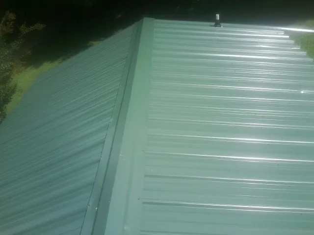 New green metal panels meeting at the ridge of a roof — Flat Roof Repair work by our crew in Burden