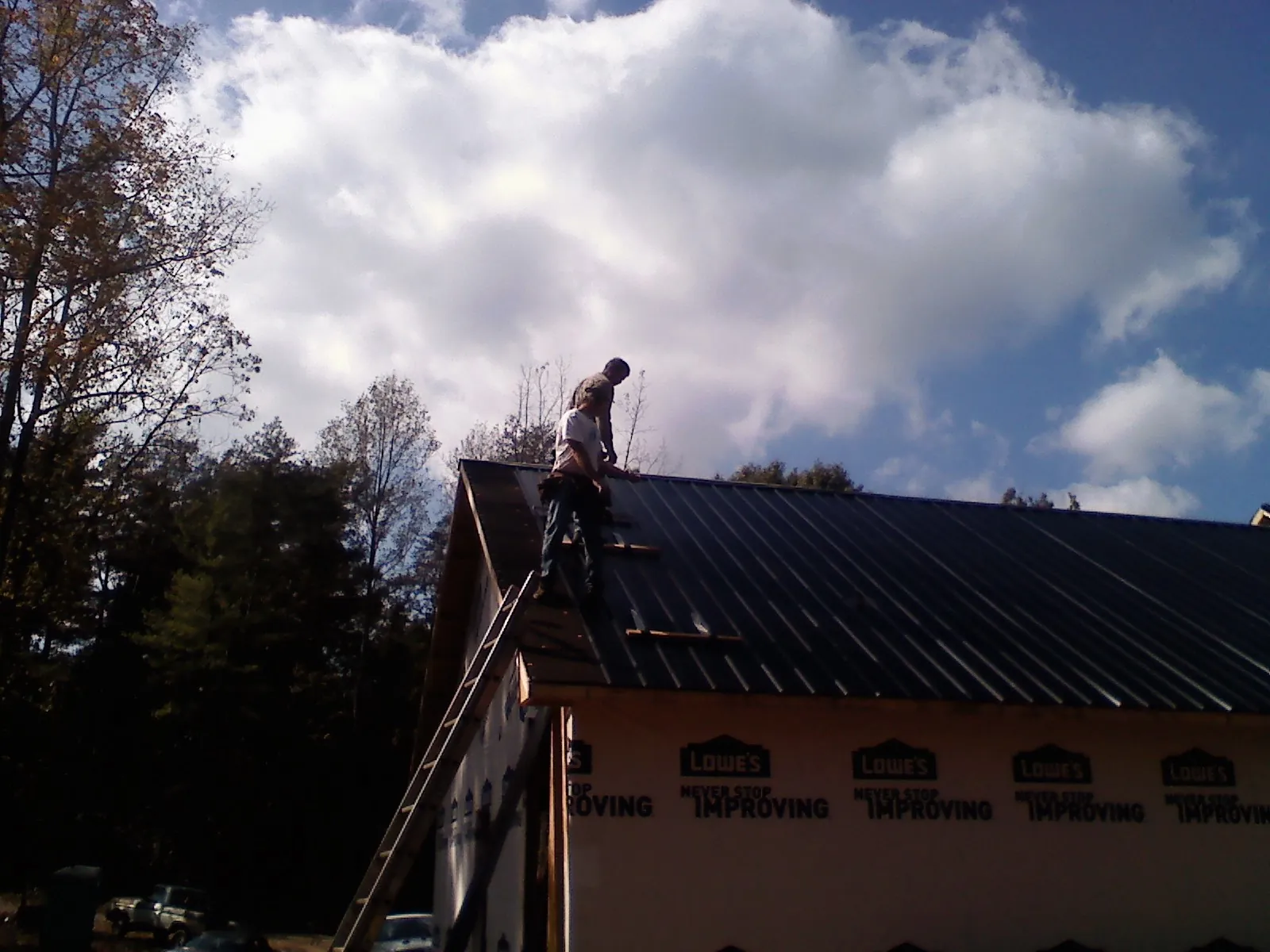 Roofer fastening dark metal panels high against a cloudy sky, from a Roof Inspection job in Burden